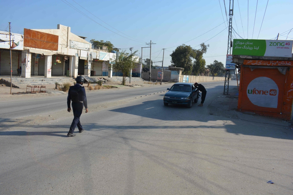 A Pakistani policeman checks a car in front of a shuttered market after Taliban militants seized a police station in Bannu on December 20, 2022. (Photo by Karim Ullah / AFP)