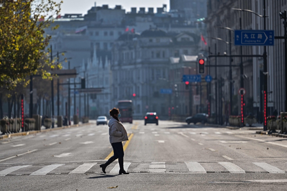 A woman crosses a street on the Bund in the Huangpu district in Shanghai on December 21, 2022. (Photo by Hector Retamal / AFP)

