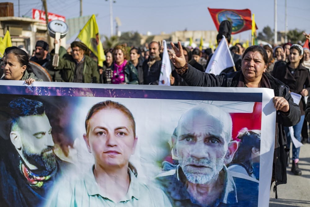 Syrian Kurds hold a banner featuring photos of three victims during a protest in Syria's northeastern city of Hasakeh on December 25, 2022 in response to a deadly attack targeting members of the ethnic community in Paris this week. Photo by Delil SOULEIMAN / AFP