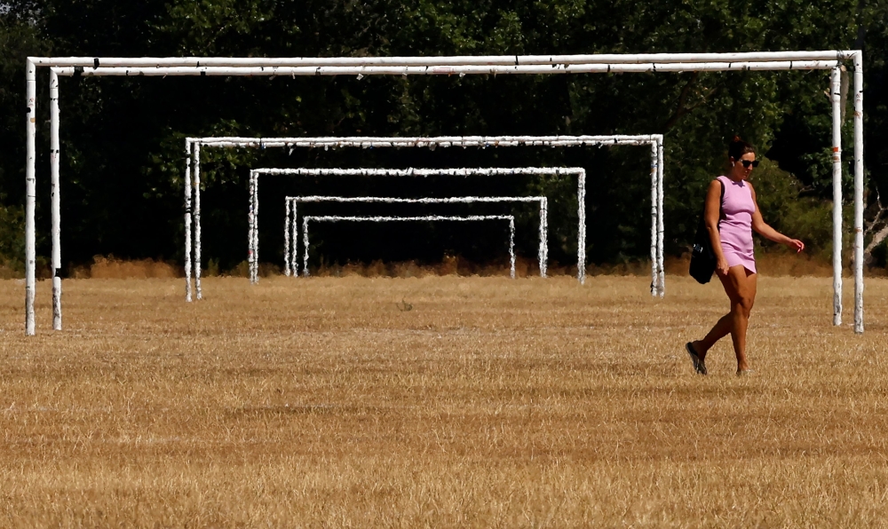 In this file photo taken on August 13, 2022 a woman walks in the heat past the goalposts on the scorched, dry grass on Hackney Marshes in London. (Photo by CARLOS JASSO / AFP)