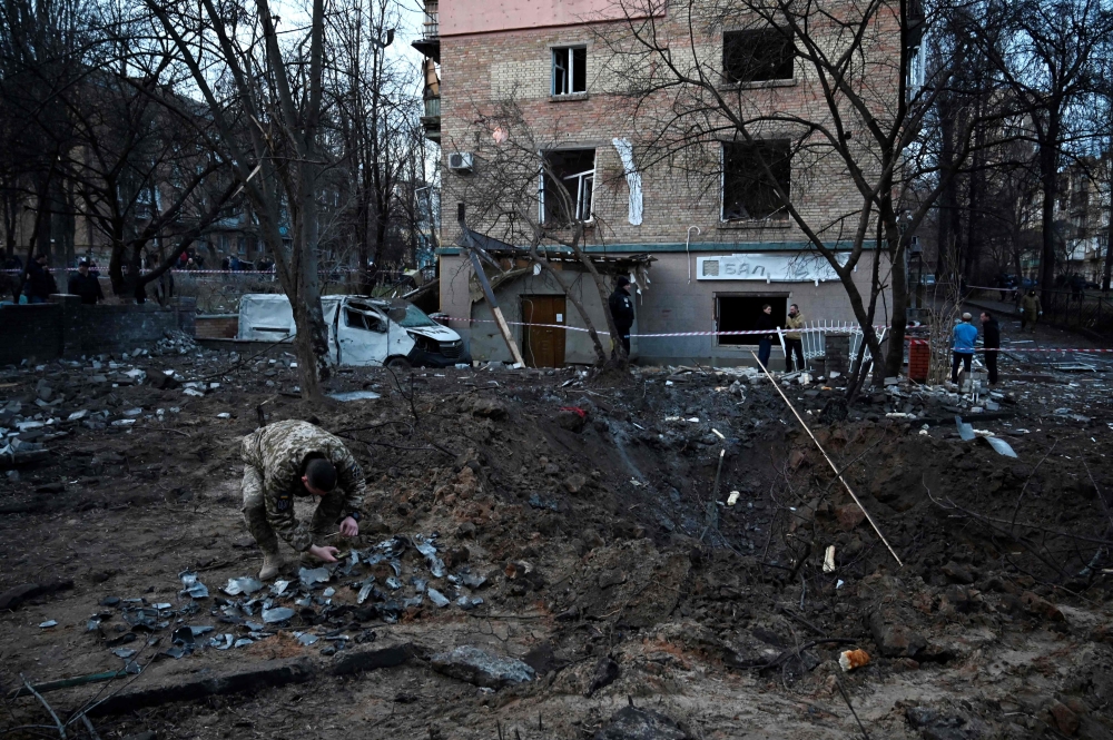 A serviceman collects fragments of missile in a crater left by a Russian strike in front of a residential building in the Ukrainian capita Kiev on December 31, 2022.  (Photo by SERGEI CHUZAVKOV / AFP)