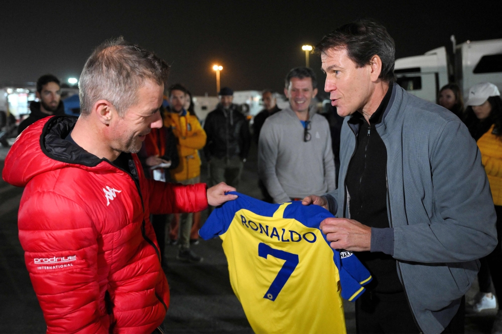 French rally driver Sebastien Loeb is presented with a Cristiano Ronaldo Al Nassr Jersey by the Saudi football club's French head coach Rudi Garcia at the bivouac in Saudi Arabia's capital Riyadh on January 8, 2023. (Photo by Franck Fife / AFP)
