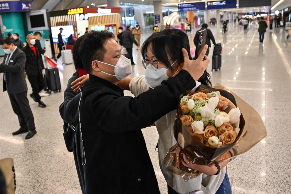 A passenger (R) receives a hug while leaving the arrival area of international flights at the Shanghai Pudong International Airport, in Shanghai on January 8, 2023.(Photo by Hector Retamal / AFP)
