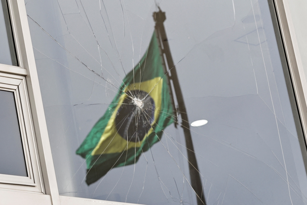 Brazil's flag is reflected on a broken window, after the supporters of Brazil's former President Jair Bolsonaro participated in an anti-democratic riot at Planalto Palace, in Brasilia, Brazil, January 9, 2023. (REUTERS/Ueslei Marcelino)