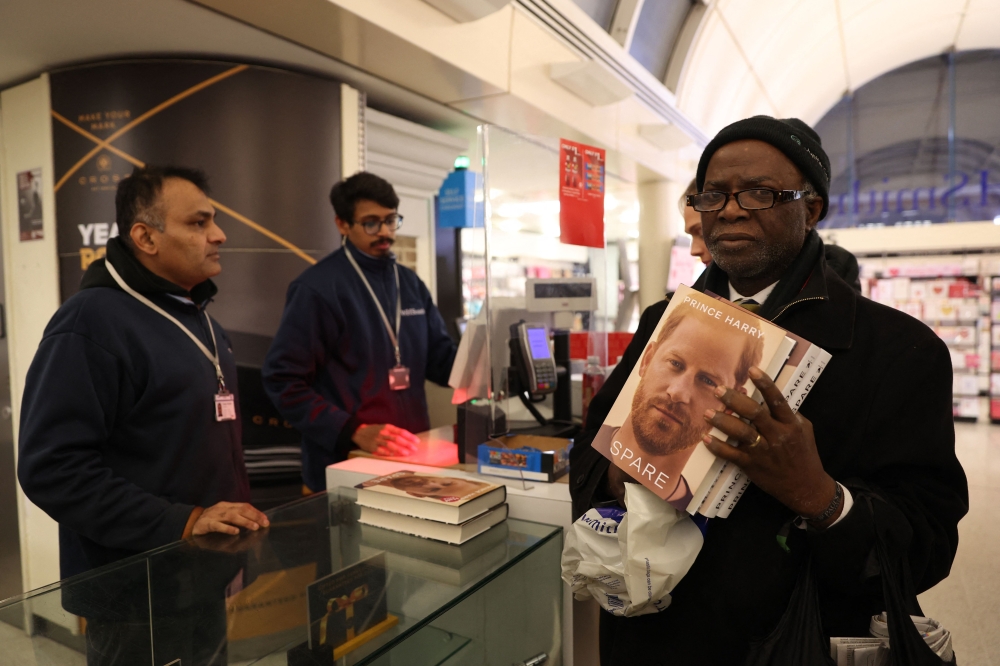 A man holds three copies of the book Spare', by Britain's Prince Harry, Duke of Sussex during a special midnight opening event for the release of the memoire, at the WHSmith bookstore, at Victoria Station in London, on January 9, 2023. (Photo by ISABEL INFANTES / AFP)