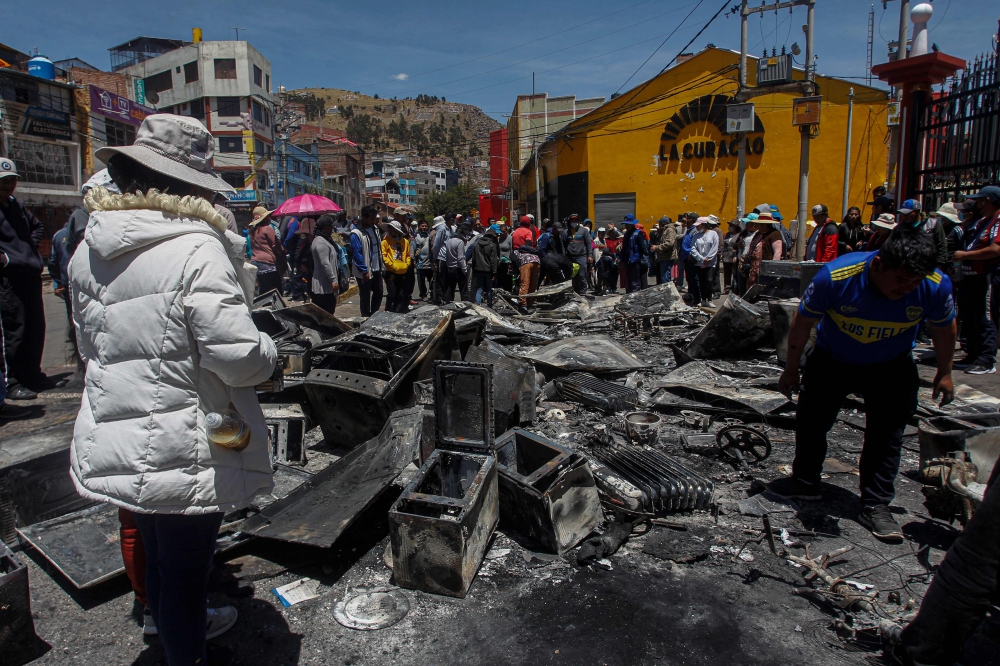 Supermarket workers inspect the fire damage in Puno, Peru, on January 10, 2023, a day after 18 people were killed in clashes between demonstrators and security forces. (Photo by Juan Carlos Cisneros / AFP)