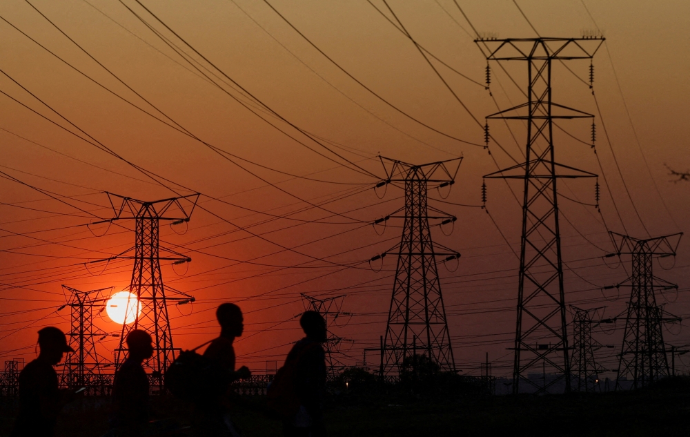 Locals walk past electricity pylons during frequent power outages from South African utility Eskom, caused by its aging coal-fired plants, in Orlando, Soweto, South Africa, on September 28, 2022.  File Photo / Reuters