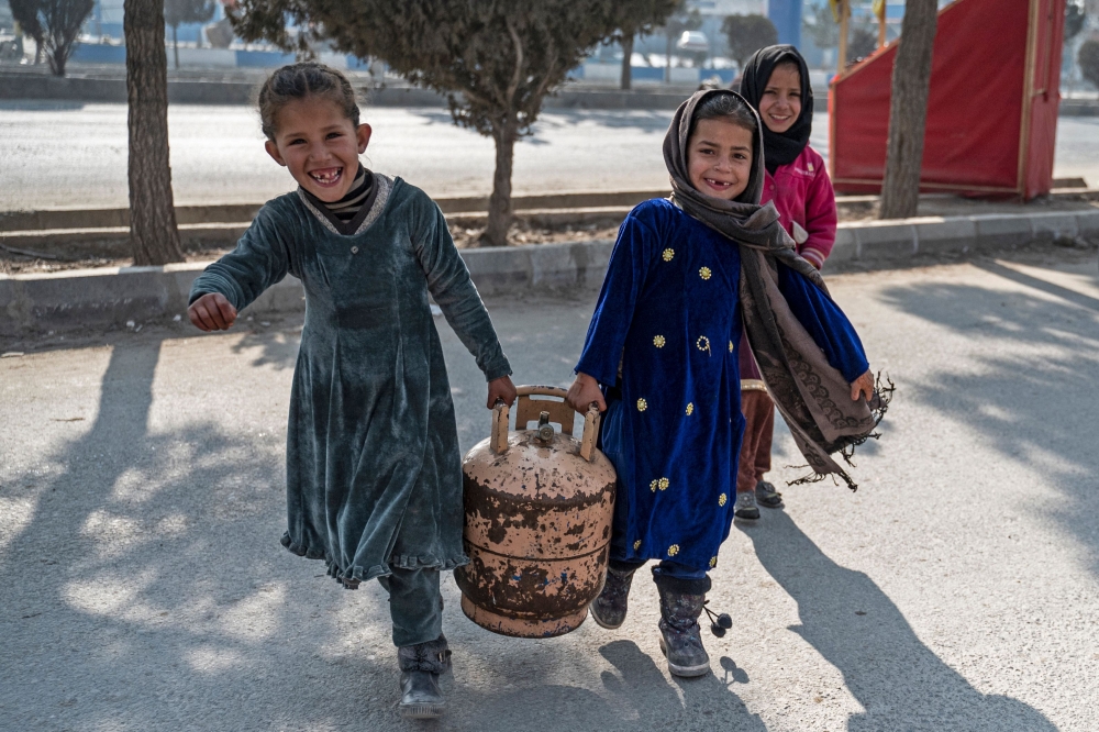 Afghan girls carry a gas cylinder along a street in Kabul on January 17, 2023. (Photo by Wakil Kohsar / AFP)
