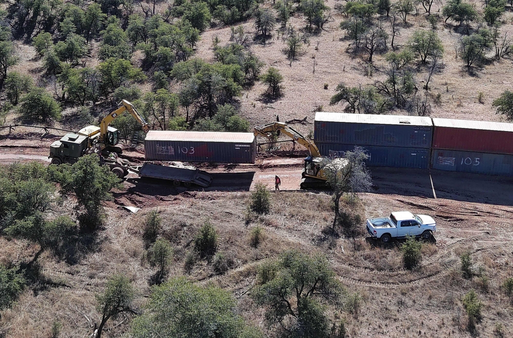 Workers watch as one of a long row of shipping containers stacked to create a wall between the United States and Mexico is lifted onto a flatbed truck for removal in the Coronado National Forest near Hereford, Arizona, on January 20, 2023. (Photo by Robyn BECK / AFP)