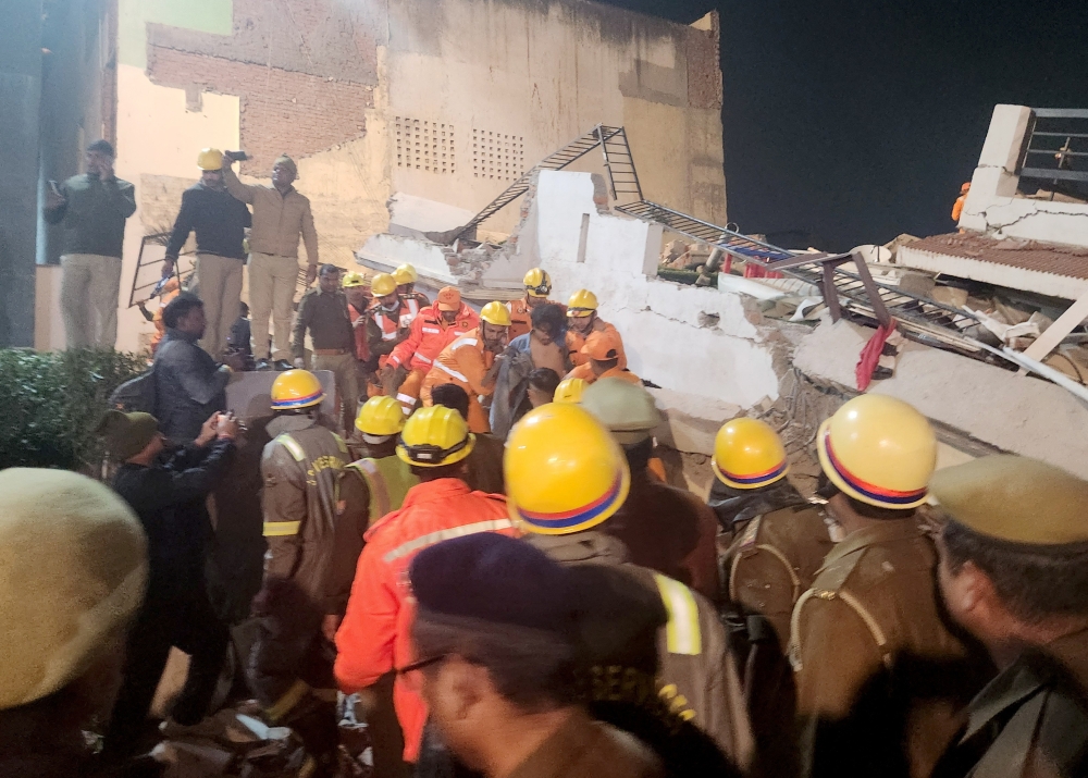 Rescue workers assist a man to a safer place after he was rescued from the debris of a collapsed residential apartment block in Lucknow, India, January 24, 2023. (REUTERS/Saurabh Sharma)