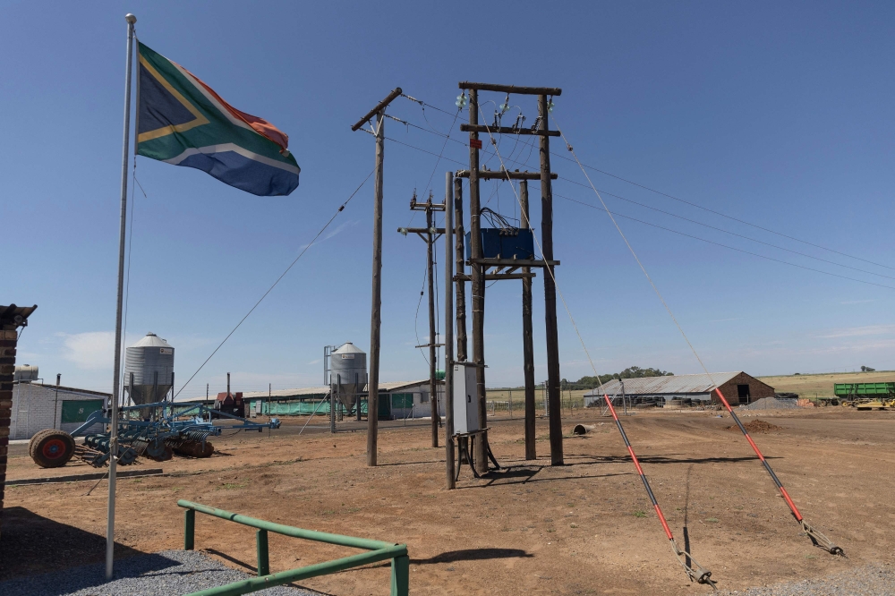A South African flag waves next to electricity poles at the Frangipani Boerdery farm near Lichtenburg on January 23, 2023. - Due to electricity disruptions an estimated of at least 40 000 of broilers died of suffocation on January 16, when insufficient voltage resulted in the air conditioning at one of the farm's chicken houses to shut down. (Photo by GUILLEM SARTORIO / AFP)
