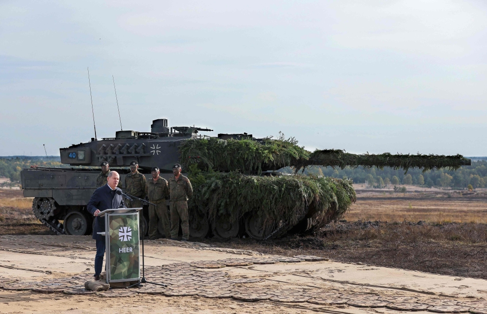 German Chancellor Olaf Scholz speaks next to a Leopard 2 battle tank of the German armed forces Bundeswehr as he visits German Bundeswehr's troops during a training exercise at the military ground in Ostenholz, northern Germany, on October 17, 2022. Germany on January 25, 2023 approved the delivery of Leopard 2 tanks to Ukraine, after weeks of pressure from Kyiv and many allies. (Photo by Ronny Hartmann / AFP)