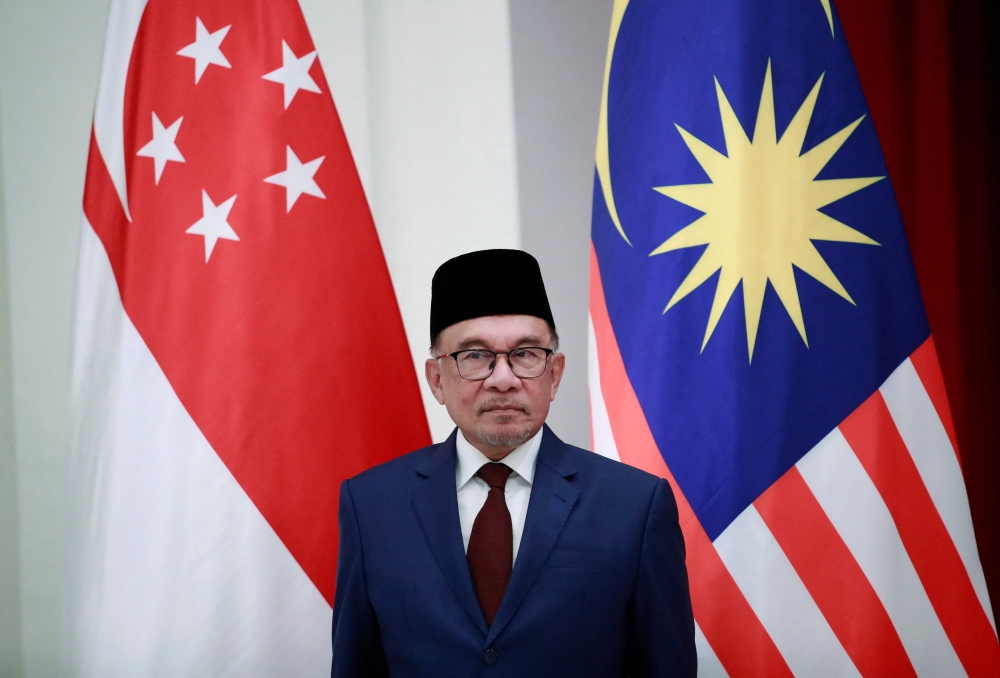 Malaysian Prime Minister Anwar Ibrahim stands in front of the Singapore (L) and Malaysian national flags during a signing ceremony at the Istana Presidential Palace in Singapore on January 30, 2023. (Photo by HOW HWEE YOUNG /AFP)