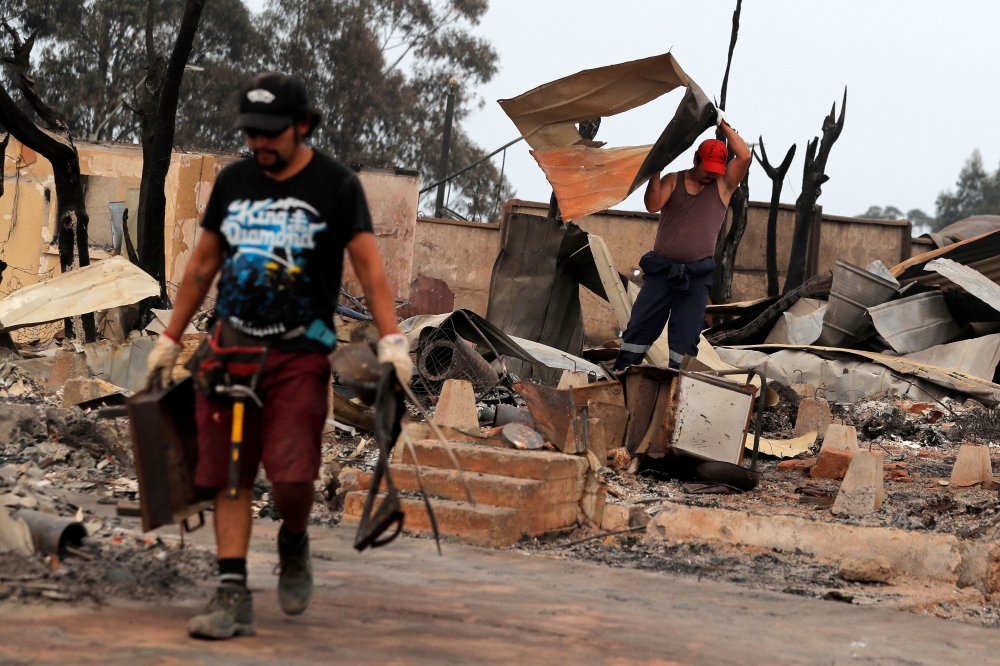 Men remove debris from houses destroyed by a forest fire in the hills of Tome, Concepcion province, Biobio region, Chile on February 4, 2023.  (Photo by JAVIER TORRES / AFP)