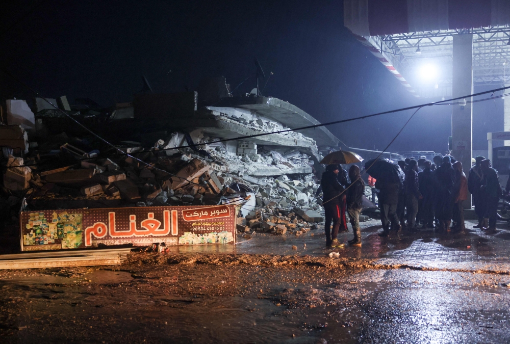 Residents gather in front of the rubble of a building that collapsed, following an earthquake in the village of Azmarin, near the Turkish border in the north of Syria's rebel-held northwestern Idlib province, early on February 6, 2023. (Photo by Omar Haj Kadour / AFP)