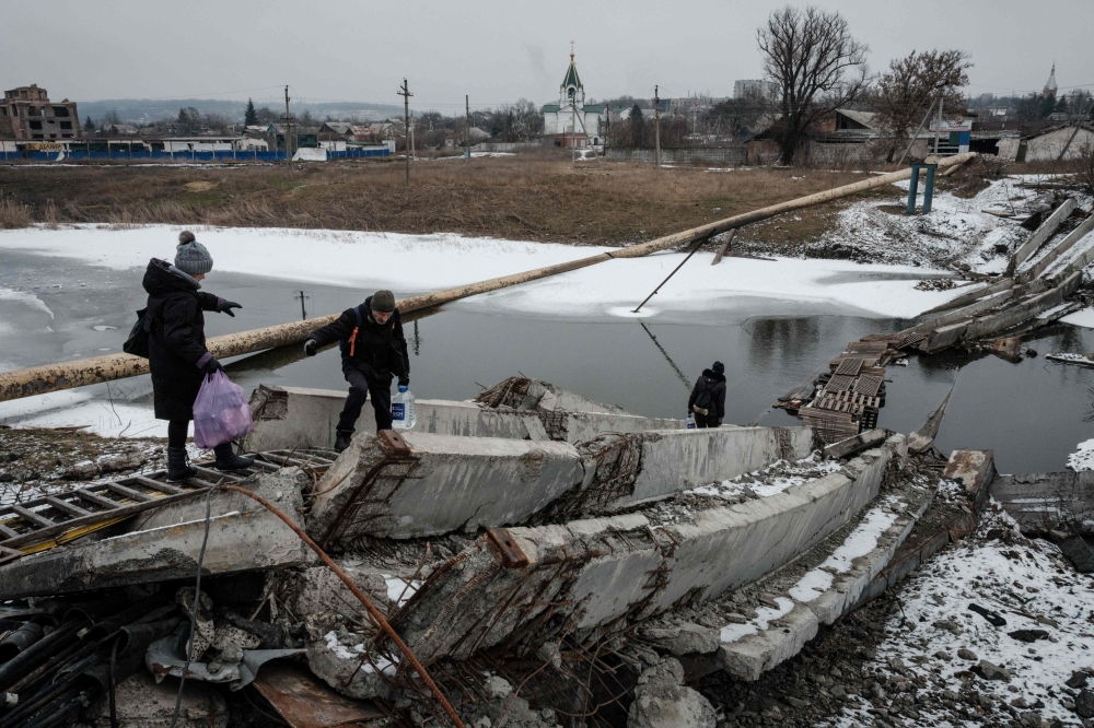 In this file photo taken on February 1, 2023 People walk on a destroyed bridge to cross a canal towards the disputed area in Bakhmut, amid the Russian invasion of Ukraine. Photo by YASUYOSHI CHIBA / AFP