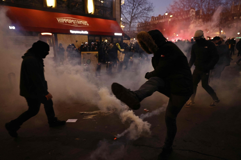 A protester kicks back a tear gas canister as clashes erupt during a demonstration on the third day of nationwide rallies and strikes against a pensions reform plan at Republique square in Paris on February 7, 2023. (Photo by Sameer Al-Doumy / AFP)