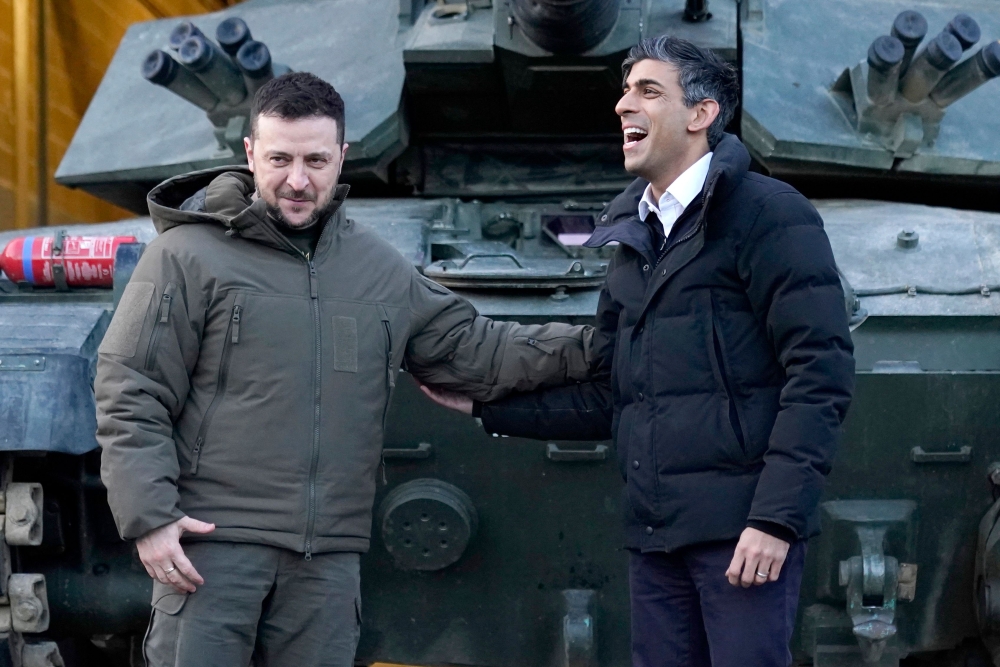 Ukraine's President Volodymyr Zelensky stands with Britain's Prime Minister Rishi Sunak as they wait to meet Ukrainian troops being trained to command Challenger 2 tanks at a military facility in Lulworth, Dorset in southern England on February 8, 2023.  (Photo by Andrew Matthews / POOL / AFP)