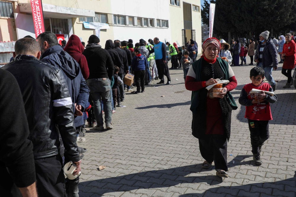 Quake-hit displaced people wait in a line to receive food at Islahiye Atatürk Stadium in Islahiye near Gaziantep on February 14, 2023, a week after a deadly earthquake struck parts of Turkey and Syria. (Photo by Zein Al RIFAI / AFP)