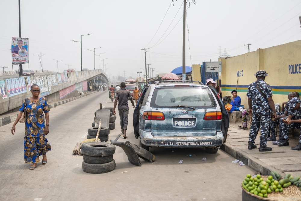 A woman walks past Nigerian police officers at a roadblock at Mile12 Market in Lagos on February 17, 2023, where violence flared up earlier in the day. - Protesters attacked bank ATMs and blocked roads in various Nigerian cities as anger spilled on the streets over a scarcity of cash. (Photo by Michele Spatari / AFP)