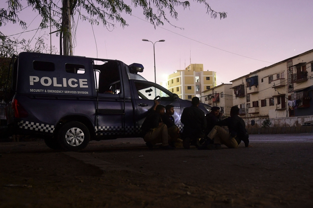 Security personnel take position behind a police vehicle near site of an attack to a police compound in Karachi on February 17, 2023. - A gunbattle was raging on February 17 night inside a Pakistan police building in the port city of Karachi, an AFP correspondent near the scene said. (Photo by Asif HASSAN / AFP)