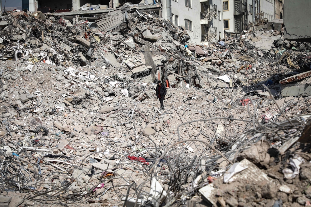 A man walks atop the rubble of collapsed buildings in Kahramanmaras, southeastern Turkey, on February 18, 2023. (Photo by Zein Al Rifai / AFP)
