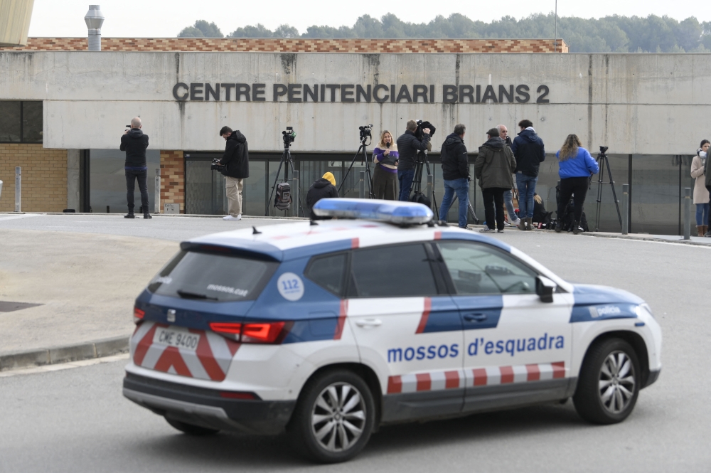 A police car is seen next to journalists informing outside the prison in San Esteve Sesrovires, 40 km from Barcelona, where Brazilian football player Dani Alves is jailed, on February 21, 2023. - Former Barcelona defender Dani Alves will remain in preventative custody pending his trial for alleged rape as he is considered a high flight risk, the Provincial Court of Barcelona decided today. (Photo by Josep LAGO / AFP)
 