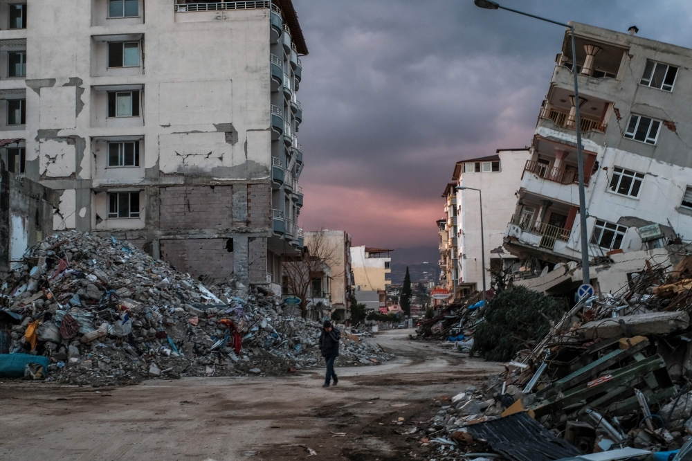 A man walks among collapsed buildings, a day after a 6.4-magnitude earthquake struck the region, in the coastal city of Samandag on February 21, 2023. Photo by BULENT KILIC / AFP
