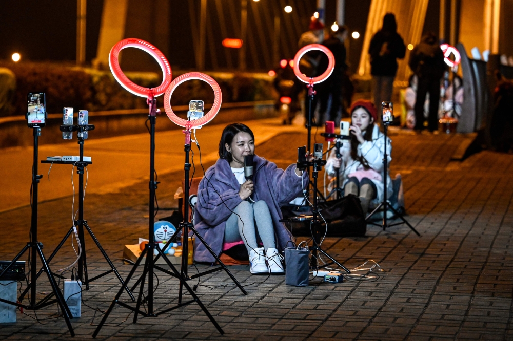 The photo taken on February 20, 2023 shows outdoor livestreamers singing and chatting with the audiences through their mobile phones on an overpass bridge at night in Guilin, in southern China's Guangxi province. Photo by Jade GAO / AFP