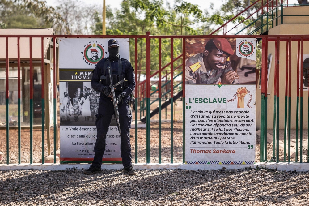 A military official stands next to a banner reflecting the face of Thomas Sankara in Ouagadougou on February 23, 2023, ahead of the reburial ceremony of Thomas Sankara's remains alongside his twelve companions, killed on October 15, 1987. (Photo by OLYMPIA DE MAISMONT / AFP)