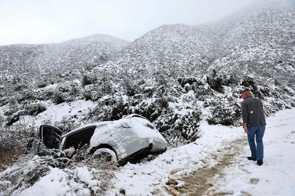 A good samaritan checks on a vehicle which skidded off the snowy roadway into a small pond in Los Angeles County, in the Sierra Pelona Mountains, on February 25, 2023 near Green Valley, California. Mario Tama/Getty Images/AFP 