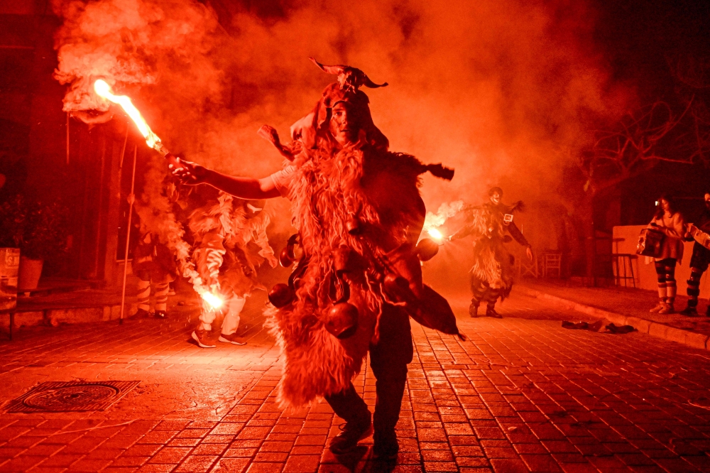 A costumed reveller lights a flare during a procession marking a traditional carnival celebration in the city of Amfissa, central Greece, on February 25, 2023. (Photo by Louisa Gouliamaki / AFP)