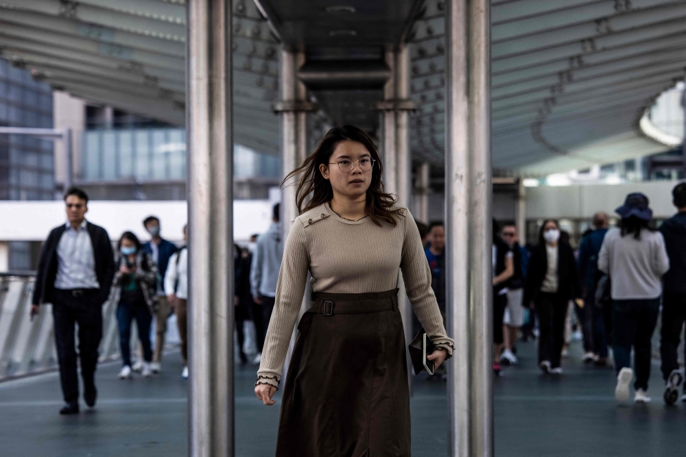 A woman (C) walks through the central business district in Hong Kong on March 1, 2023, as the government lifted a mask mandate on March 1. (Photo by ISAAC LAWRENCE / AFP)