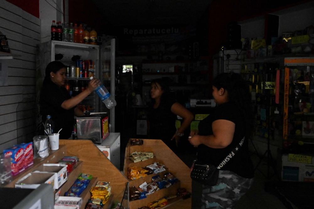 A woman buys water at shop in the dark in Buenos Aires on March 1st, 2023, following an outage caused by a fire which affected the high-voltage system.  (Photo by Luis ROBAYO / AFP)