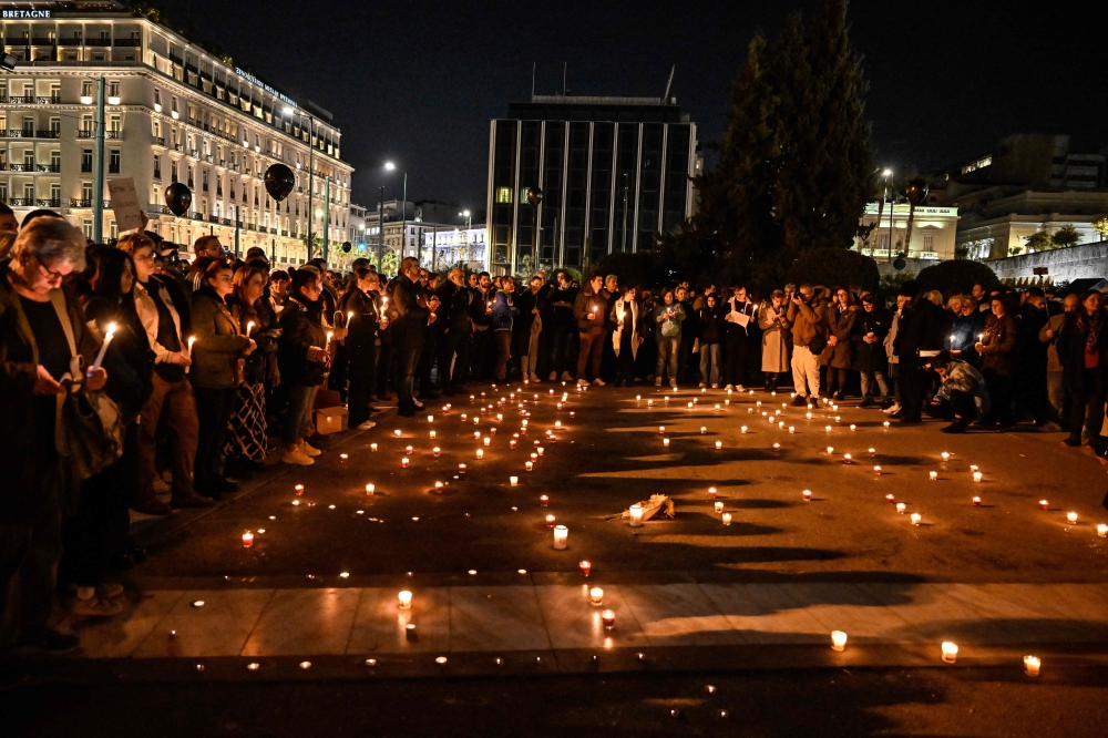 People hold candles and black balloons during a silent demonstration in front of the Greek Parliament in Athens, on March 3, 2023 (Photo by Louisa Gouliamaki / AFP)