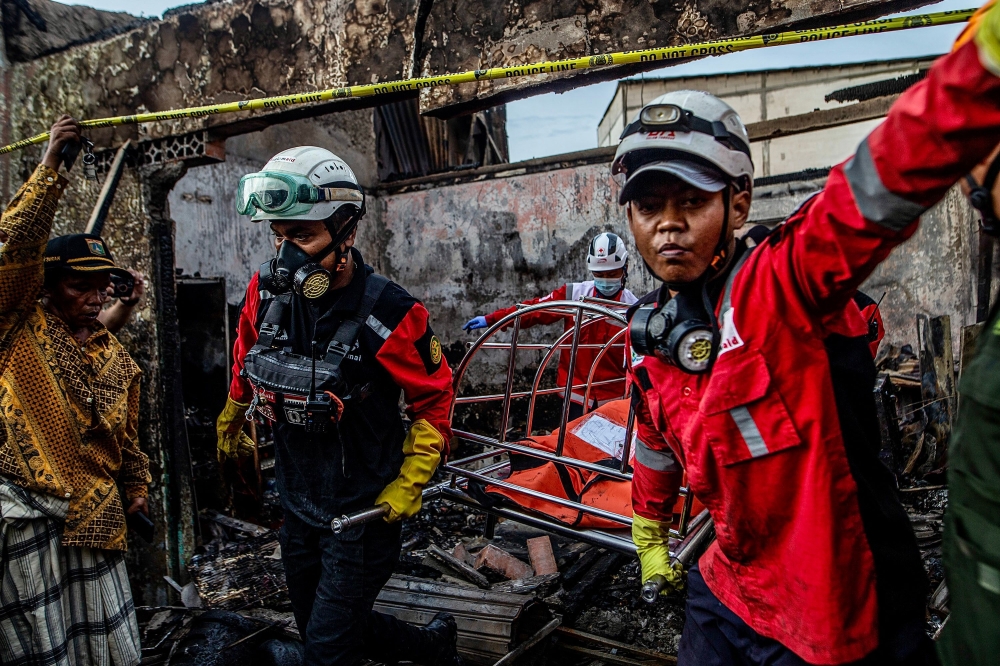 Firefighters evacuate a victim's body from a house in a residential area in Plumpang, north Jakarta on March 4, 2023, after a fire at a nearby state-run fuel storage depot run by energy firm Pertamina. Photos by ADITYA AJI / AFP