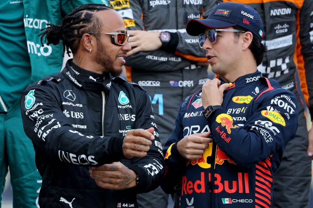 Mercedes' British driver Lewis Hamilton (left) speaks with Red Bull Racing's Mexican driver Sergio Perez during a group photo opportunity with other racers ahead of the Bahrain Formula One Grand Prix at the Bahrain International Circuit in Sakhir on March 5, 2023. (Photo by Giuseppe CACACE / AFP)