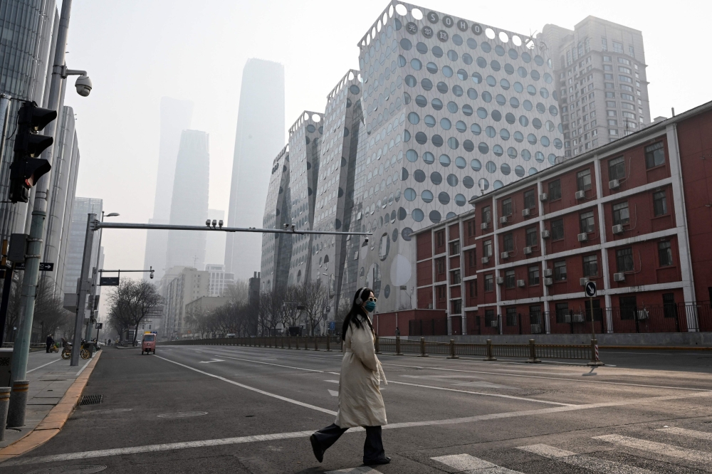 A woman crosses a street at central business district in Beijing on March 5, 2023 (Photo by Jade Gao / AFP)