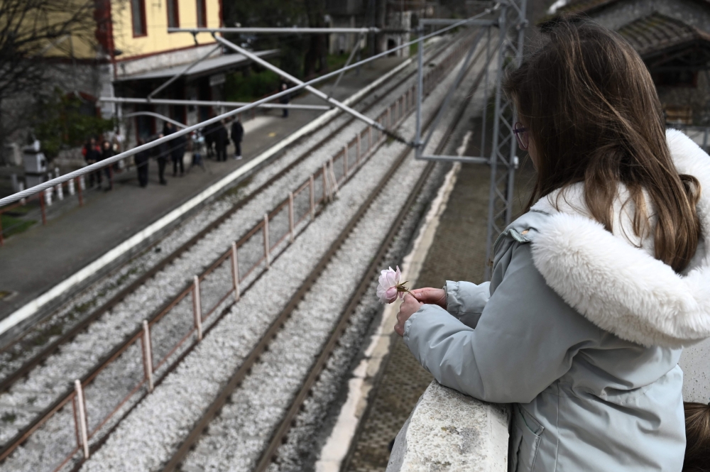 A girl holds a flower at the railway station of Rapsani, north Greece, on March 5, 2023, during a commemorative gathering for the victims of a deadly train crash which killed 57. Photo by Sakis MITROLIDIS / AFP