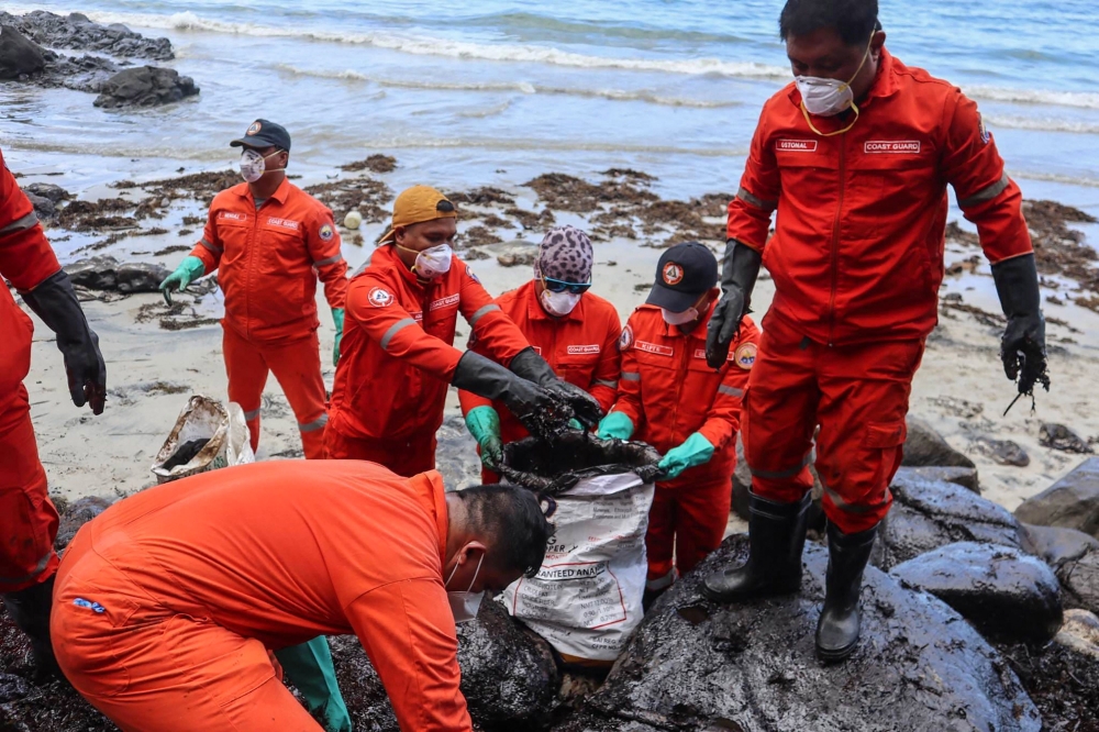 This handout photo taken on March 8, 2023 and released by the Philippine Coast Guard (PCG) shows coast guard personnel and volunteers collecting debris covered with oil during a clean-up along the coast in Pola, Oriental Mindoro Province, days after an oil spill from a sunken tanker. (Photo by Handout / Philippine Coast Guard (PCG) / AFP)