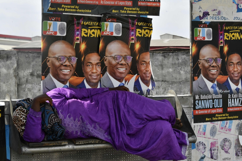 A woman lies beside campaign posters of Lagos gubernatorial candidate of the ruling All Progressives Congress (APC) Babajide Sanwo-Olu and runningmate Obafemi Hamzat displayed at a bus station in Lagos, on March 7, 2023 ahead of March 11 gubernatorial elections.  (Photo by PIUS UTOMI EKPEI / AFP)