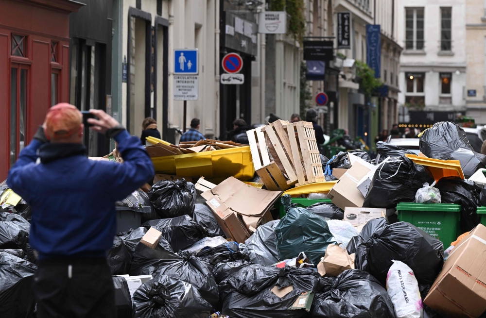 A pedestrian takes a picture of household waste containers in a street of Paris, on March 12, 2023, which have been piling up since collectors went on strike against the French government's proposed pensions reform on March 6, 2023. (Photo by Stefano RELLANDINI / AFP)