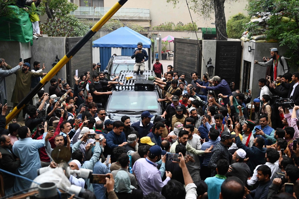Supporters of former Pakistan's Prime Minister Imran Khan gather around his car as he leaves his residence in Lahore on March 18, 2023, on his way to appear in a court in Islamabad. (Photo by Aamir Qureshi / AFP)
