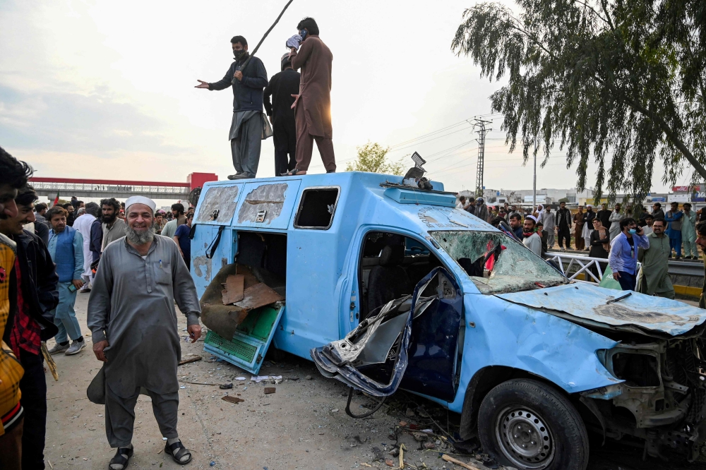 Pakistan's former Prime Minister Imran Khan's supporters stand atop a damaged police van outside a court in Islamabad on March 18, 2023. (Photo by Farooq NAEEM / AFP)