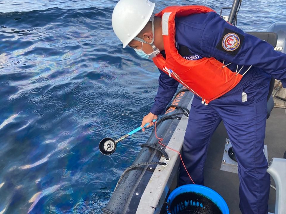 In this handout photo received from the Philippine Coast Guard and taken on March 2, 2023, a coast guard personnel collects water sample from of an oil spill in the waters off Naujan, Oriental Mindoro. Photo by Handout / Philippine Coast Guard (PCG) / AFP

