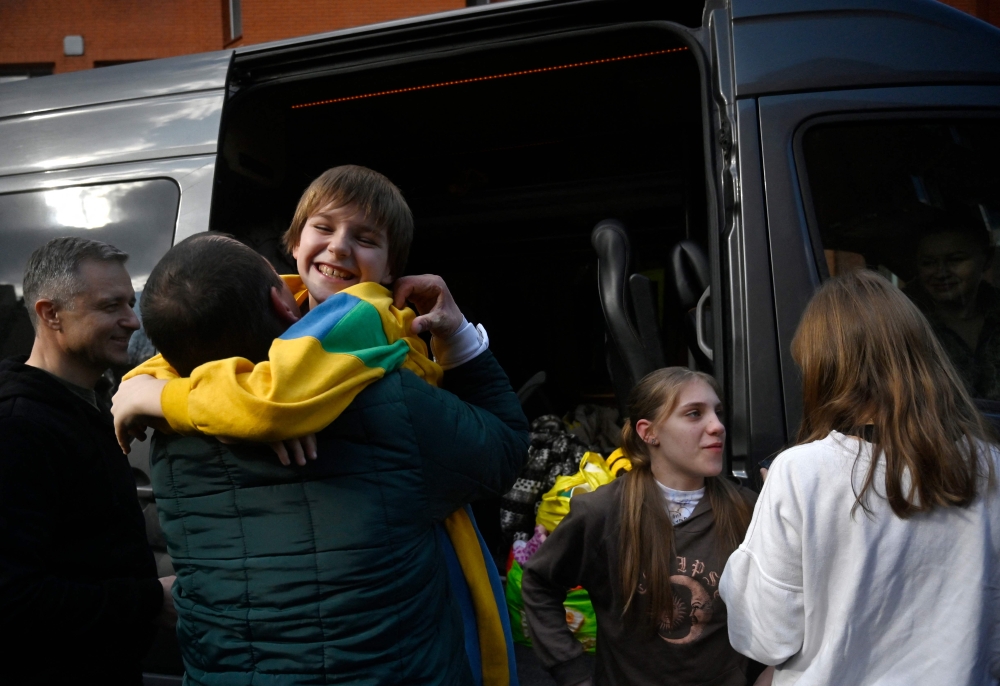 Denys Zaporozhchenko (left) meets his children Nikita, Yana and Dayana (right) after the bus delivering them and more than a dozen other children back from Russian-held territory arrived in Kyiv on March 22, 2023.  (Photo by SERGEI CHUZAVKOV / AFP)