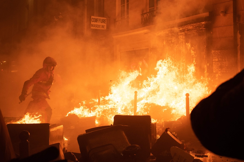 A firefighter tries to extinguish a fire during a demonstration, a week after the government pushed a pensions reform through parliament without a vote, using the article 49.3 of the constitution, in Paris on March 23, 2023. (Photo by Anna Kurth / AFP)