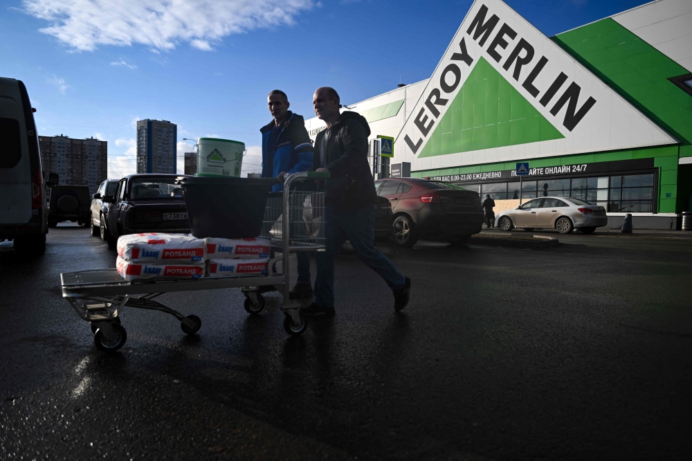 Men walk with a cart loaded with purchases on a parking lot of a Leroy Merlin DIY store in the Moscow region, some 50 km off Moscow, on March 24, 2023. (Photo by NATALIA KOLESNIKOVA / AFP)