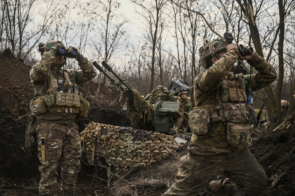 Ukrainian servicemen (L and R) look on with binoculars next to another (C) sitting on an anti-air gun near Bakhmut, on March 24, 2023. (Photo by Aris Messinis / AFP)
 