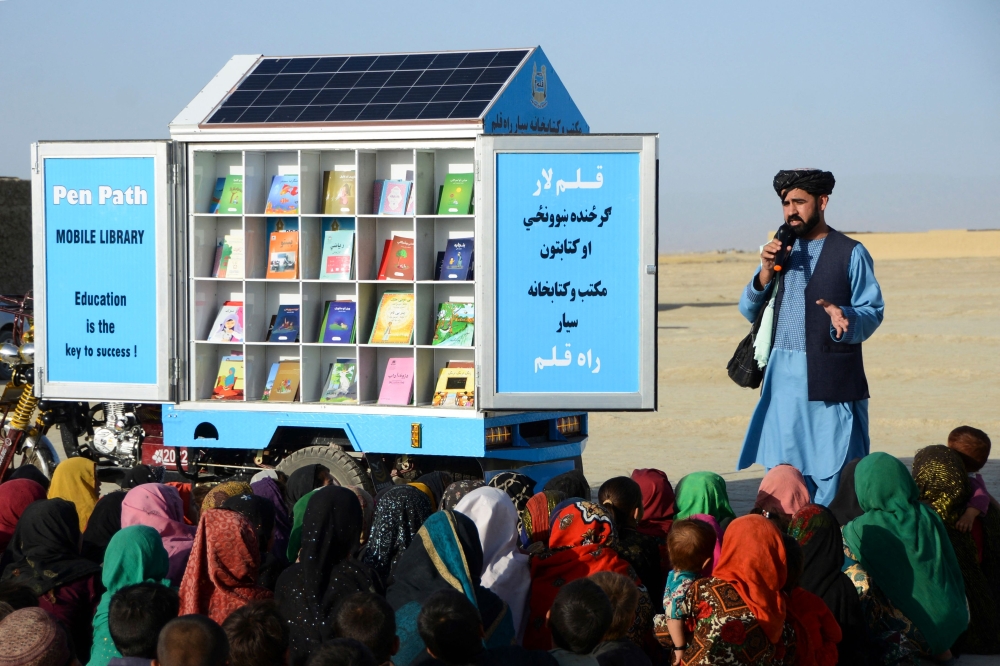 In this photograph taken on May 17, 2022, Matiullah Wesa, head of PenPath and advocate for girls' education in Afghanistan, speaks to children during a class next to his mobile library in the Spin Boldak district of Kandahar Province. (Photo by Sanaullah Seiam / AFP)
